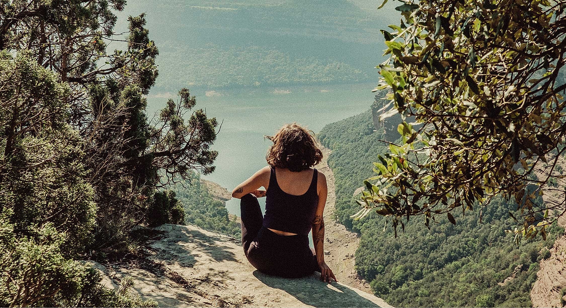 Person sitting on a cliff overlooking a lake.
